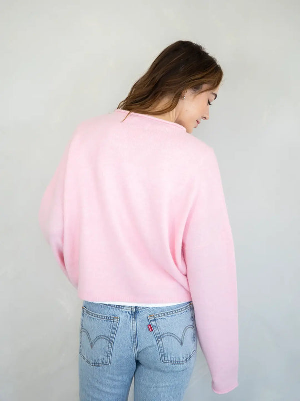 Person wearing a pink sweater and light blue jeans against a plain background