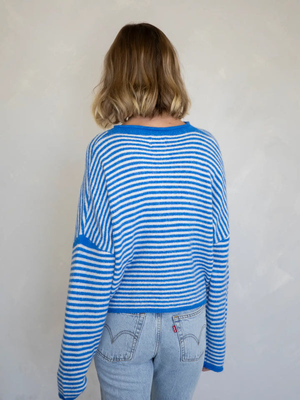 Person wearing a blue and white striped sweater and light blue jeans against a plain background