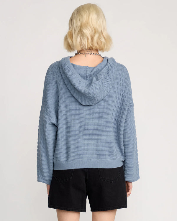 Person wearing a blue hooded sweater and black shorts on a plain background
