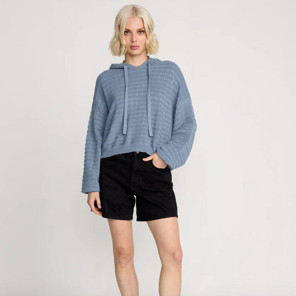 Person wearing a blue sweater, black shorts, and black boots on a light gray background