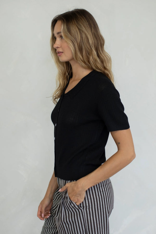 Woman wearing a black top and striped pants against a plain background
