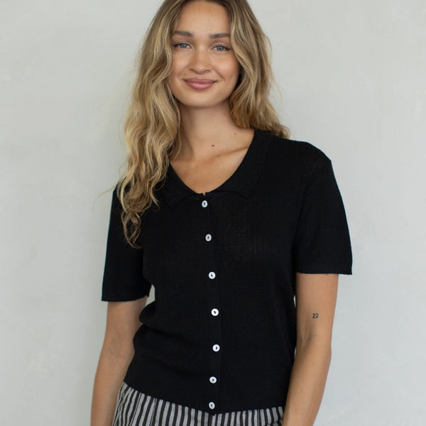Woman wearing a black button-up shirt and striped pants against a plain background