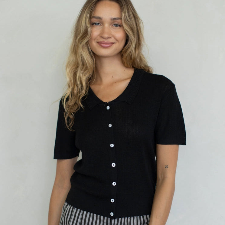 Woman wearing a black button-up shirt and striped pants against a plain background