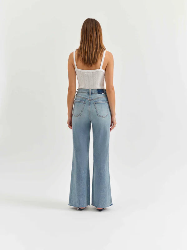 Woman wearing light blue jeans and a white top on a plain background