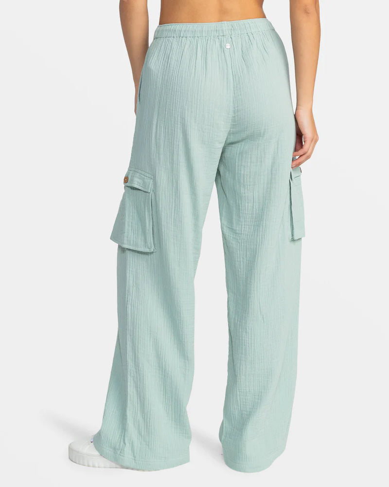 back view of the model wearing the precious beach high waist cargo pants. shows the elastic waistband. also shows the wide leg, the side cargo pockets with the coconut button closure. 