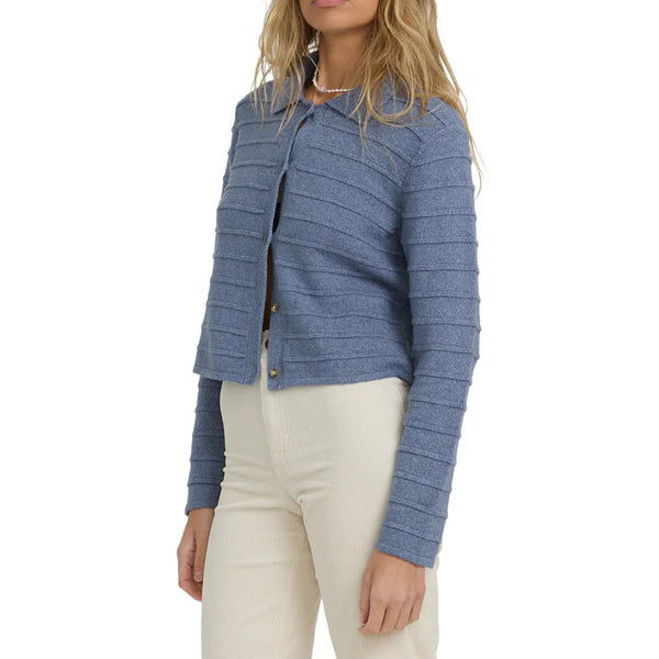 model wearing a blue cardigan with button down closure, collar with cream pants against a white background. 