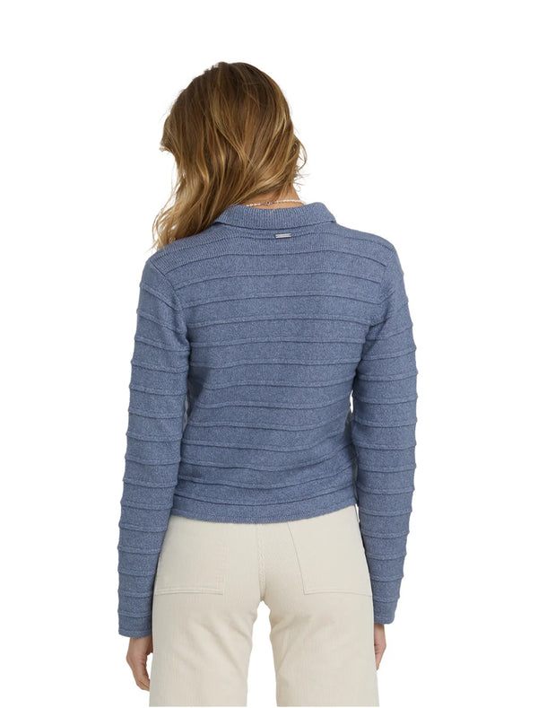 model wearing blue cardigan with cream pants against a white background.