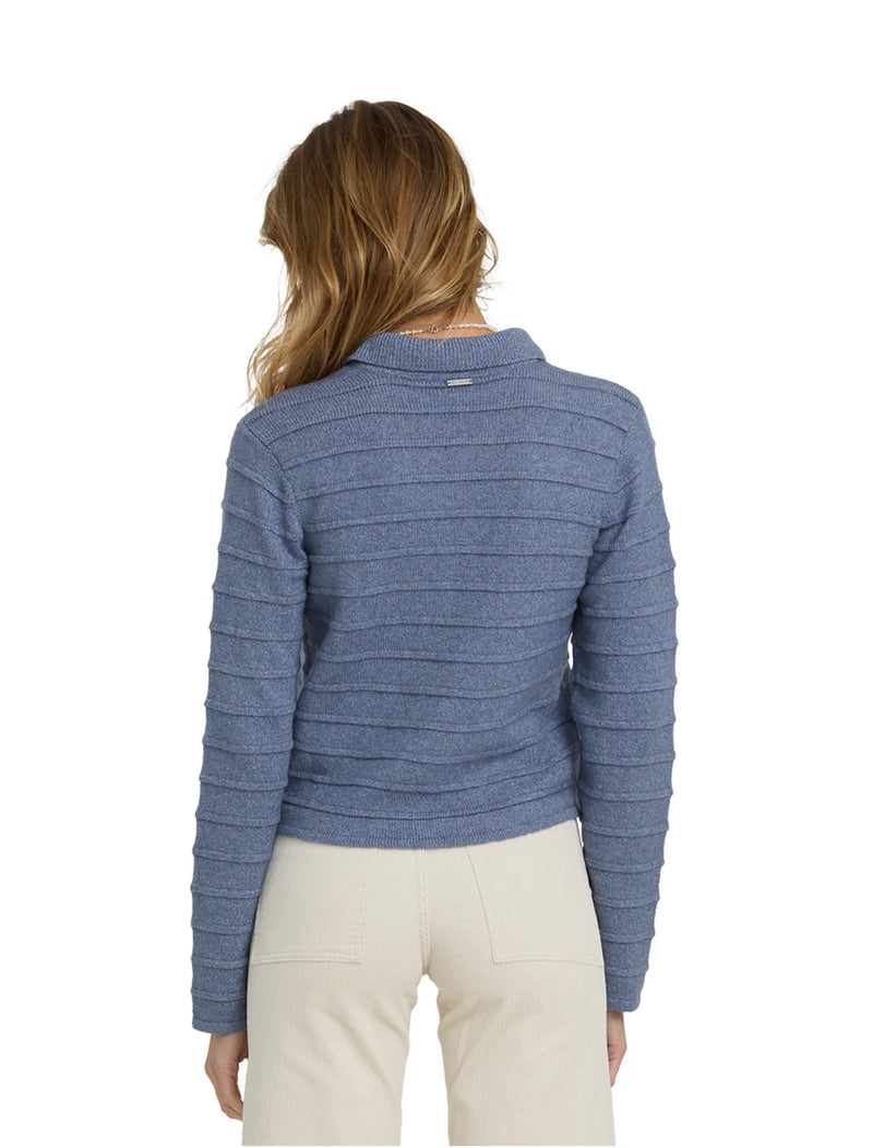 model wearing blue cardigan with cream pants against a white background.
