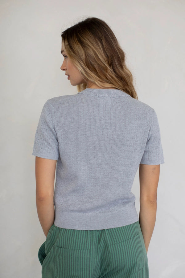 Woman wearing a light gray sweater and green pants against a plain background