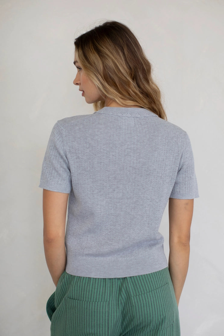 Woman wearing a light gray sweater and green pants against a plain background