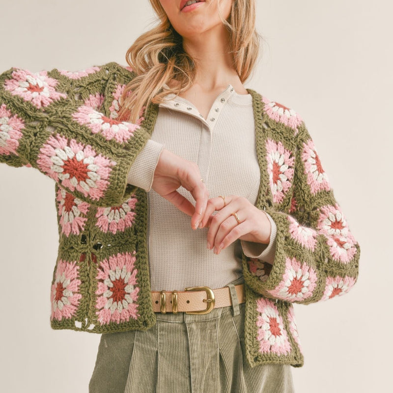 Front view of model wearing daisy cards. Shows the open front with the crochet daisies. Also shows that the cardigan is cropped and has long sleeves. 