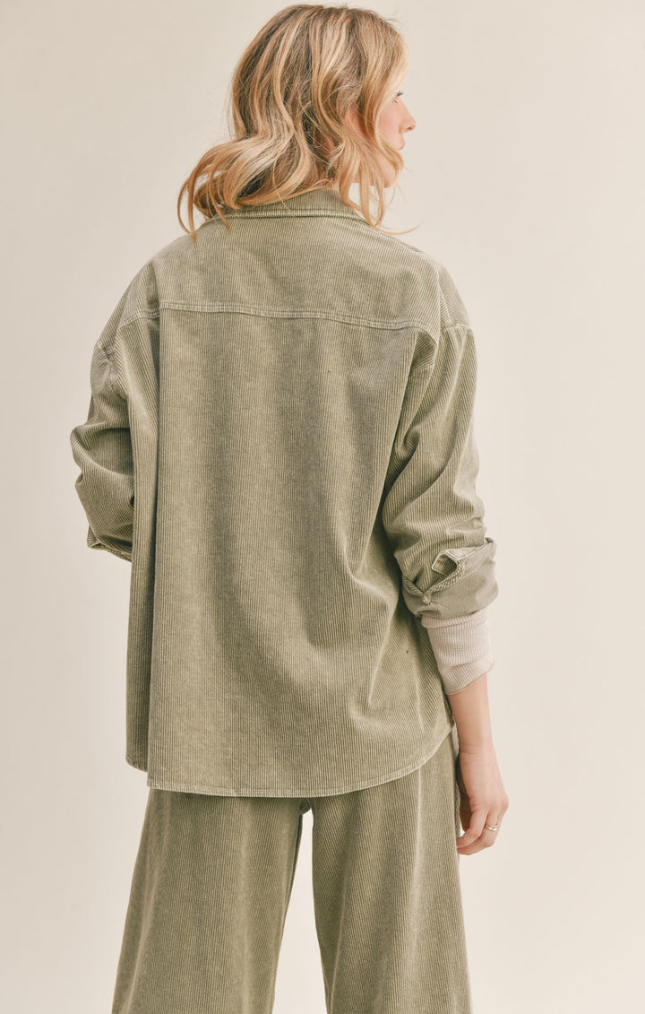 Back view of model wearing shacket. Shows the drop hem. Also shows the long sleeves and back view of the collar and the beautiful sage corduroy look. 