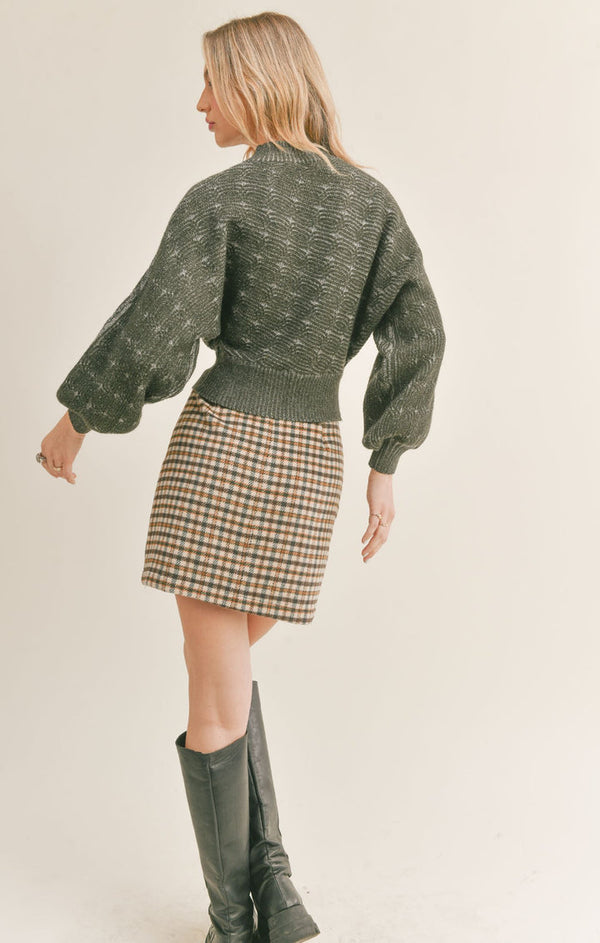 Back view of the model wearing the plaid skirt. Shows the skirt is mini and high waisted. Also shows the brown multi coloring plaid. 