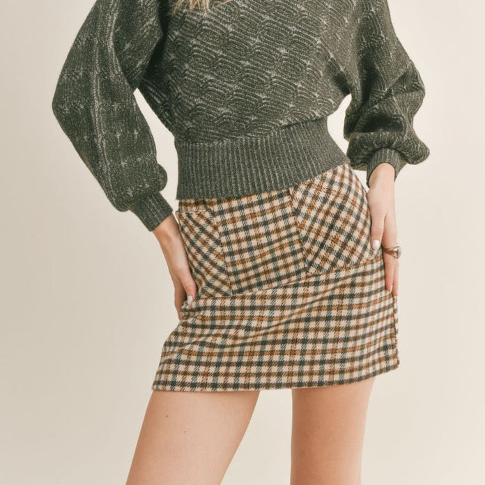 Front view of the model wearing skirt. Shows the front pockets and that the plaid on the pockets are going a different direction then the rest of the plaid on the skirt. Also shows that the skirt is mini and high waisted. 