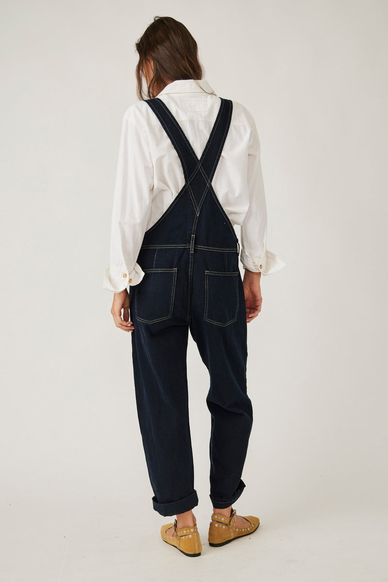 back view of model in overalls. here you can see the thick straps and back pouch pockets. as well as the tapered legs and white contrast seam details.