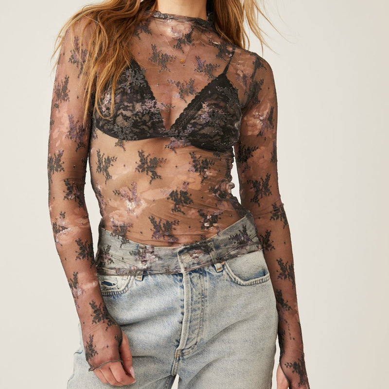 front view of model wearing top. showcases the sheer fabrication with a high neck, and the thumbholes are visible. there are little floral print placed throughout the shirt.