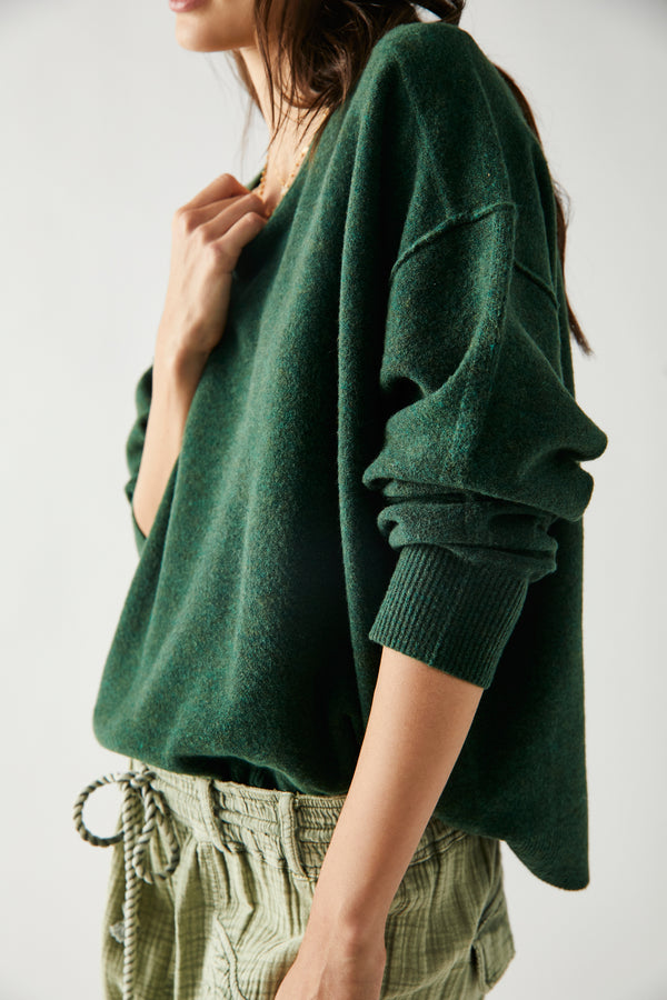 Side view of model wearing pullover. Shows the dropped shoulders. Also shows the exposed seaming and the ribbed detailing on the cuff. 