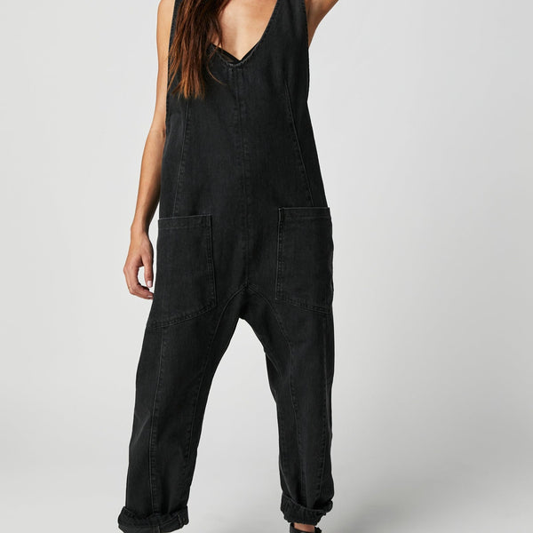 Front view of model wearing jumpsuit. Shows the low scoop neckline. The front oversized patch pockets, ankle length, drop-crotch harem-style legs, detailed seaming throughout and the beautiful mineral washblack color. 
