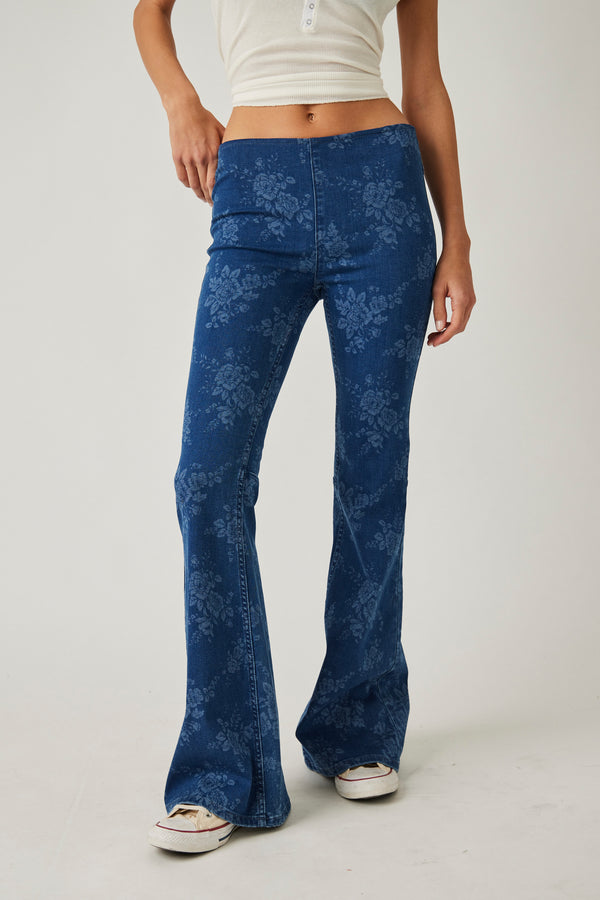 another front view of model in jeans. mid rise waist is visible, hits model below belly button. there's a center seam down the front and wide, long legs with a faded white floral print all over.