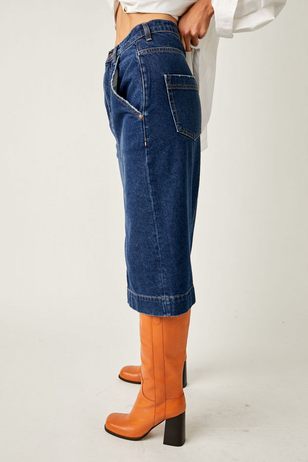 shows side view of model in skirt. here you can see the side pockets as well as the back pockets, the midi length and rigid denim fabrication.