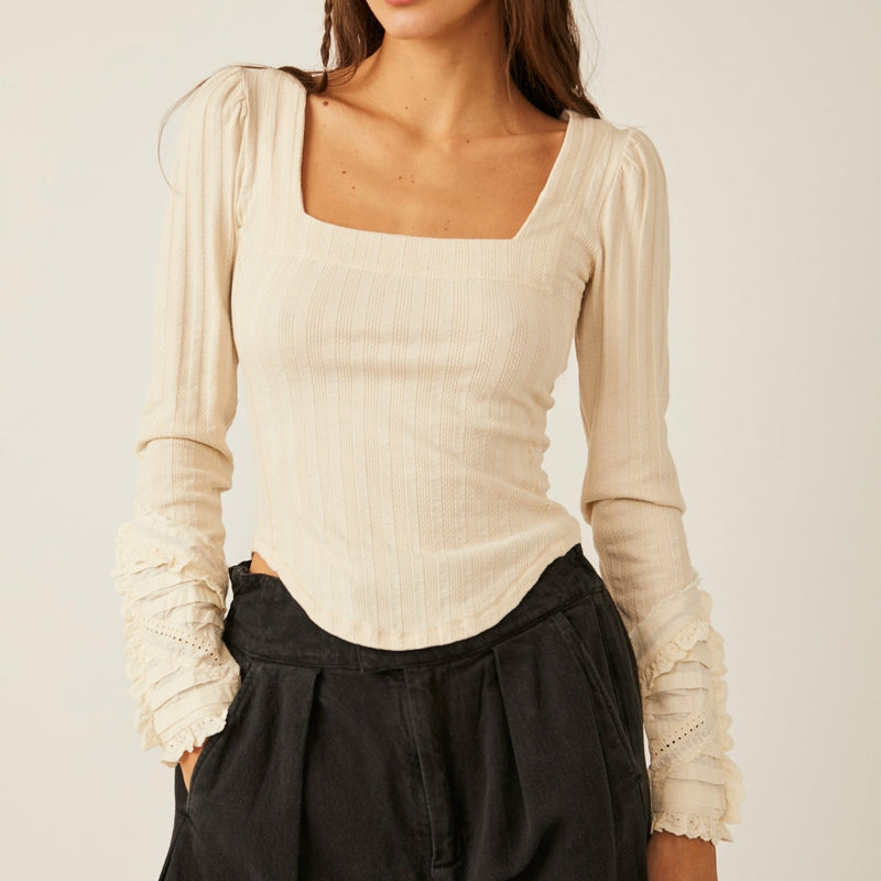 front view of model in top. shows the square neckline, ruffled shoulders and lace cuffs. the rounded bottom hemline is visible as well. 