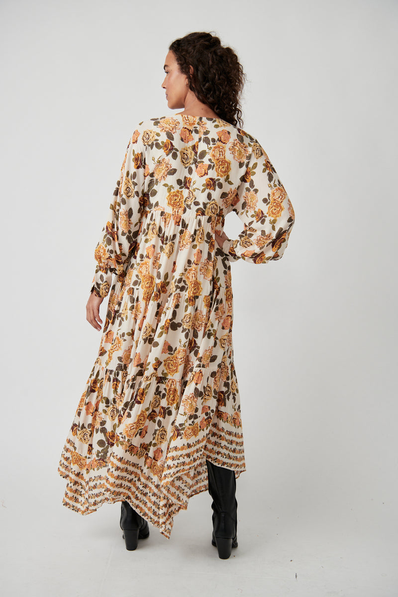 back view of model in dress. shows all over floral print and flowy long skirt. asymmetrical hemline is visible.