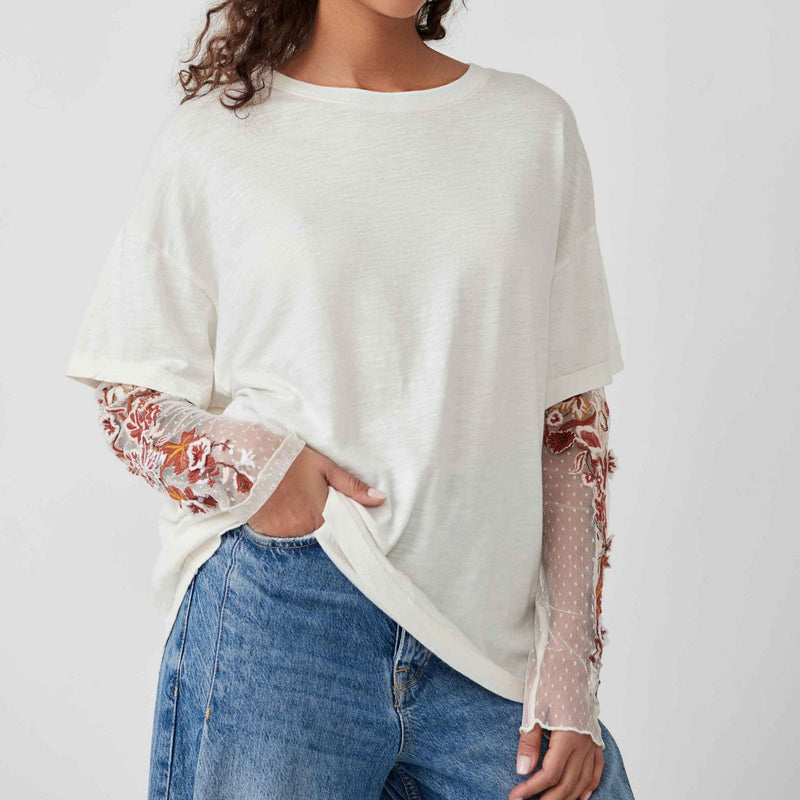 shows front view of model wearing white color top. shows a t-shirt overlay with a crew neckline and oversized fit. showcases sheer sleeves with floral embroidery. 