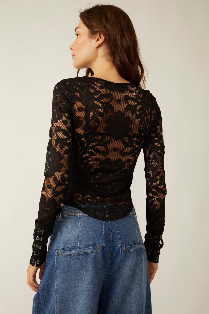 Back view of model wearing top. Shows the scoop neckline.  The mesh/lace floral detailing, the rounded bottom hem and the color of the shirt is black. 