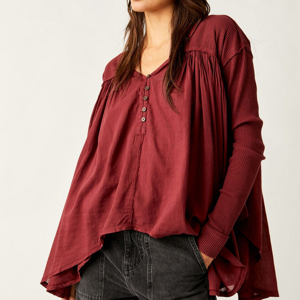 Front view of the model wearing top. Shows button down closure neckline. SHows the ribbed detailing on the sleeves, the slouchy relaxed fit, the handkerchief bottom hem, the color of the top is red/wine color called mulberries. 
