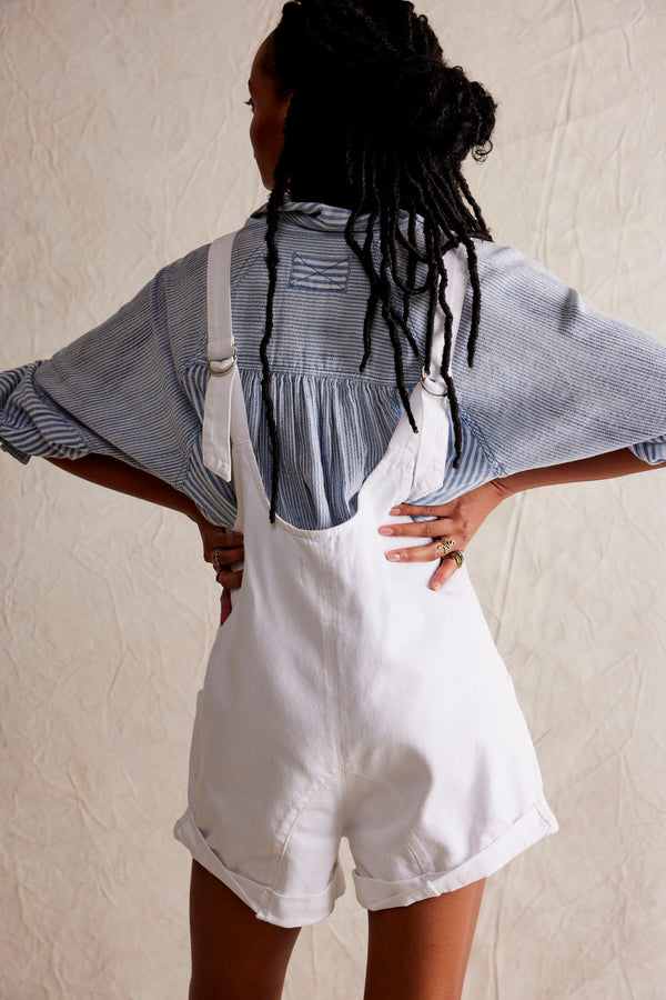 back view of the model wearing the high roller shortall. shows the low back scoop neckline. also shows the adjustable straps, the slouchy fit and the bottom rolled cuffs. 