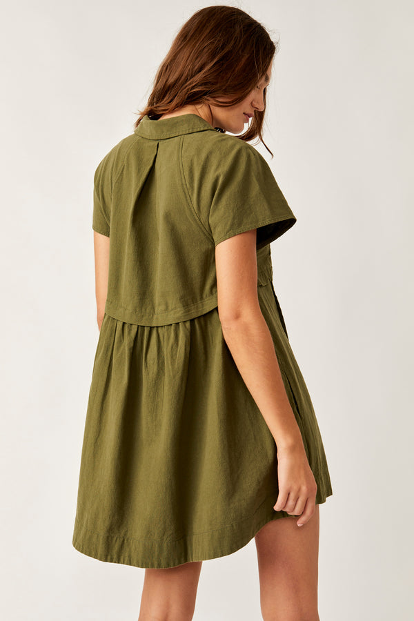back view of the model wearing the ronnie poplin mini dress. shows the short sleeves. also shows that the dress is alittle longer in the back than front and shows the over lap detail around the waist, 