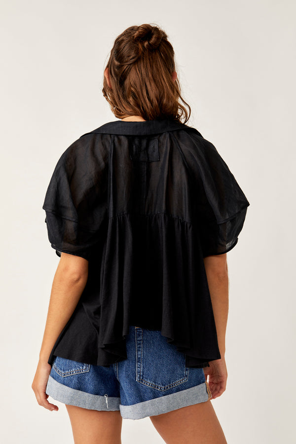 back view of model wearing the sunray babydoll top. shows the puffy sleeves. also shows the asymmetrical hem and exposed seaming detail.  