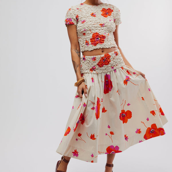 front view of the model wearing the carino printed set. shows the smocking through the top and top portion of the skirt. the skirt is an a-line silhouette. The top is slim fitting and a crew neckline. the skirt is a pull on style with the midi length. 