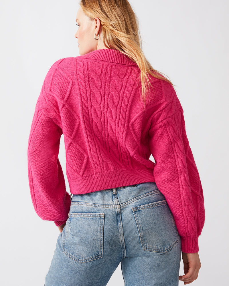 Back view of model wearing sweater. Shows the back being a slight longer than front. Also shows the cable knit detail and balloon sleeves. 