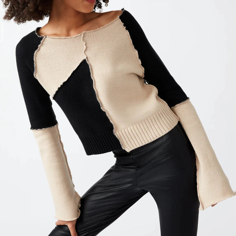 Front view of model wearing sweater. Shows the wide raw edge boat neck. Also shows the exposed shows the asymmetrical  hem and the exposed overlock seams. Also shows the bell sleeves. 