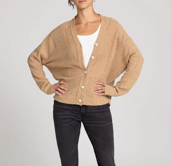 Person wearing a beige cardigan over a white shirt with black pants on a light gray background