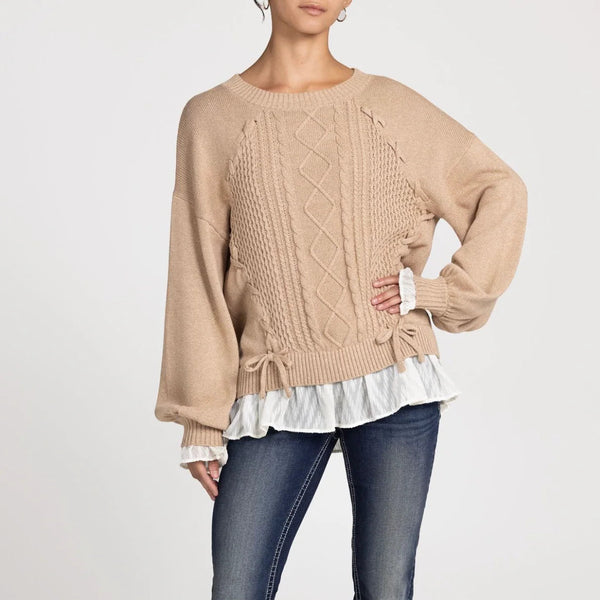 Beige cable knit sweater with ruffled hem worn by a person on a white background