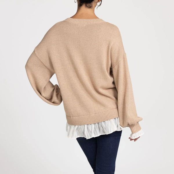 Person wearing a beige sweater over a white top with a plain background