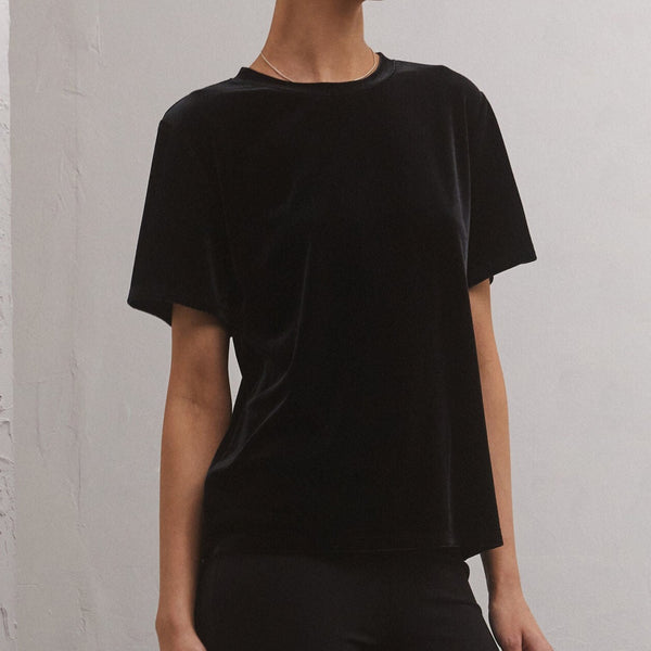 front view of model wearing the Simone velvet top in black. shows the crew neckline. also shows the short sleeves, the velvet detail and that the shirt hits right below the waist. 