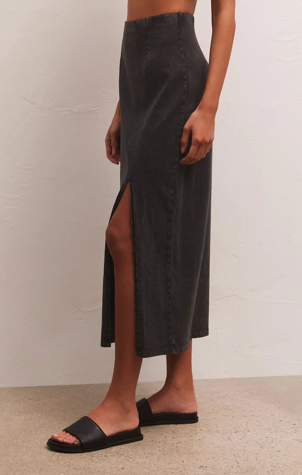 side view of model in skirt. shows the high waist, visible seams, side slit and cropped length, hits model at mid calf.