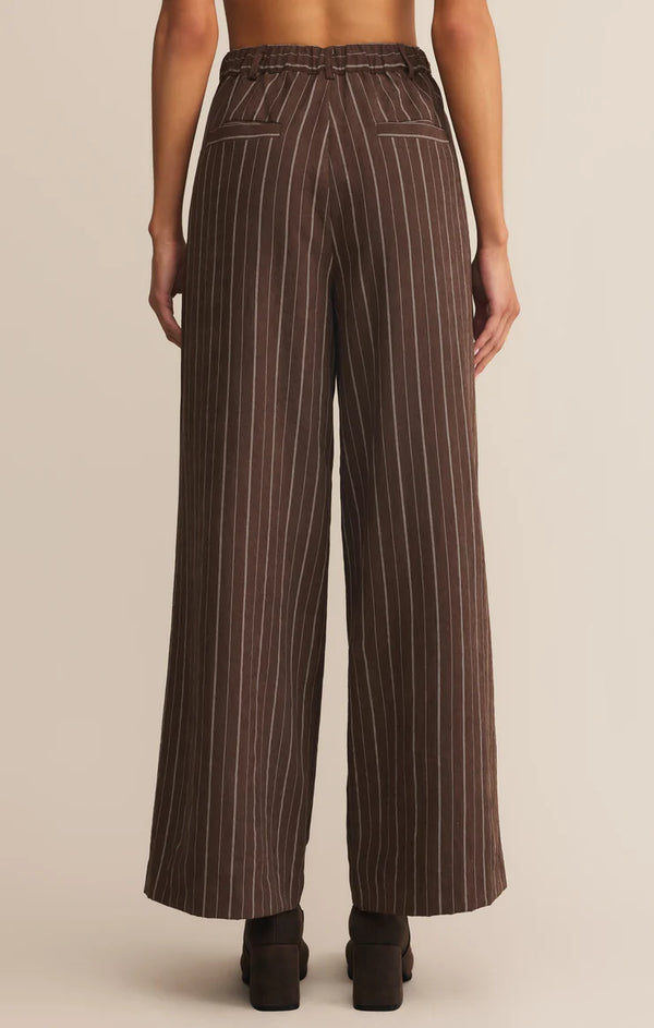 Brown pinstripe pants worn by a person on a beige background