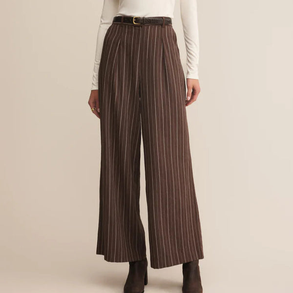 Woman wearing a white top and brown striped pants on a beige background