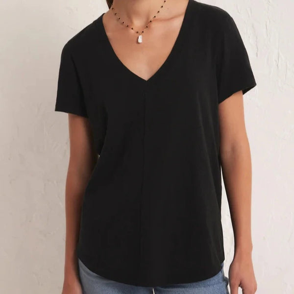 front view of the model wearing the asher v neck tee in black. shows the relaxed fit. also shows the v neckline, the curved bottom hem and the raw hems detailing throughout. 
