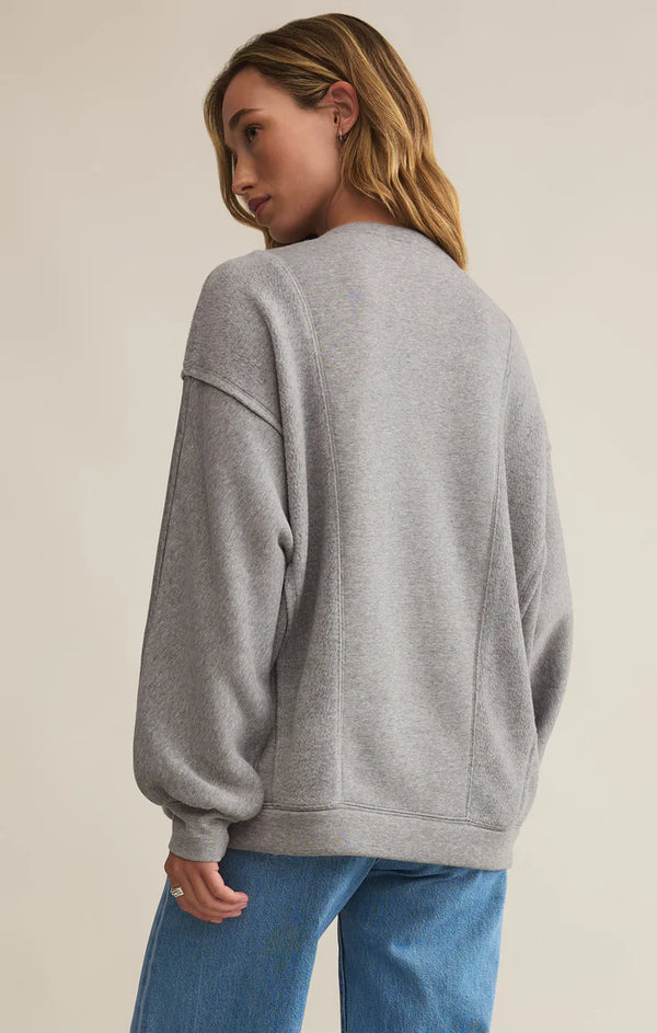 back view of the model wearing the out of towner sweatshirt. shows the dropped shoulders. also shows the exposed seams, the relaxed fit and the heather grey color. 