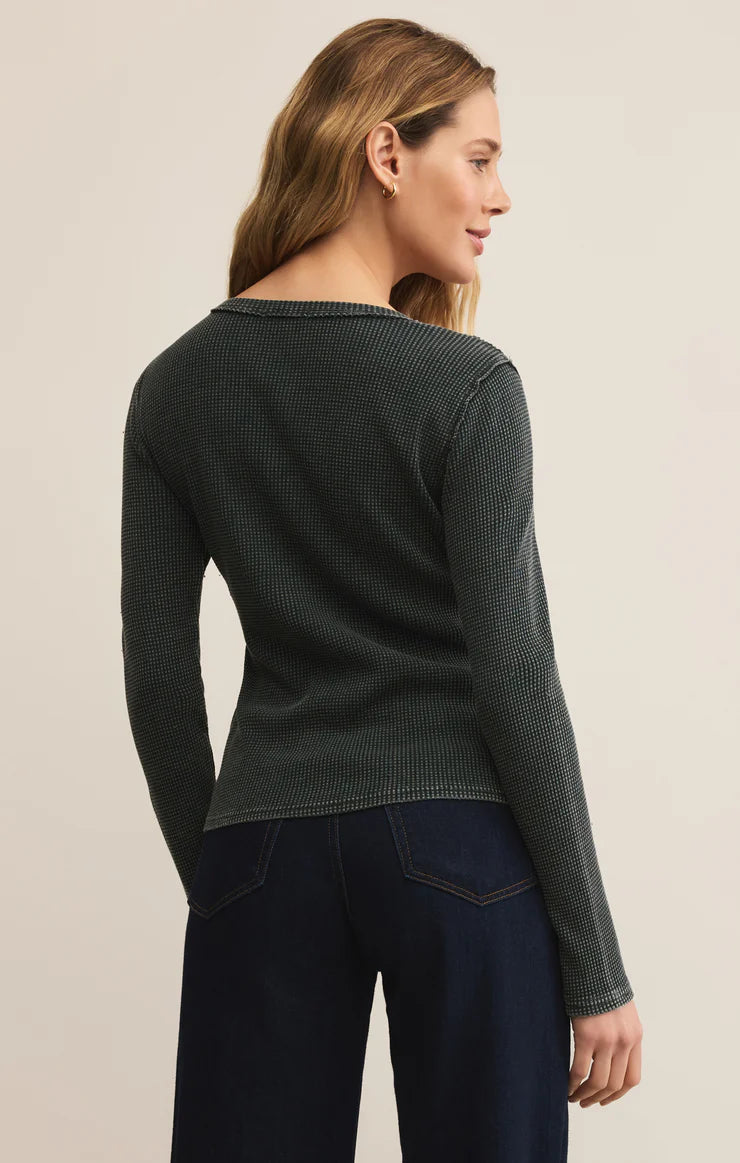 Woman wearing a dark green sweater and dark blue pants on a beige background