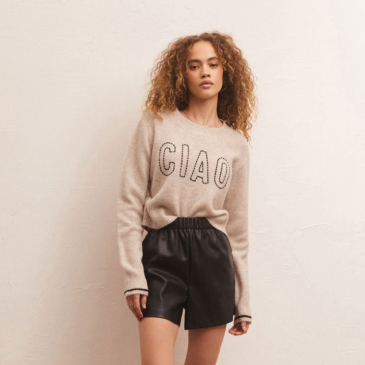 front view of model in sweater. shows the crew neckline, contrast stripe detail on sleeves and chain stitch "ciao" lettering. model as the front of the sweater tucked into her shorts.