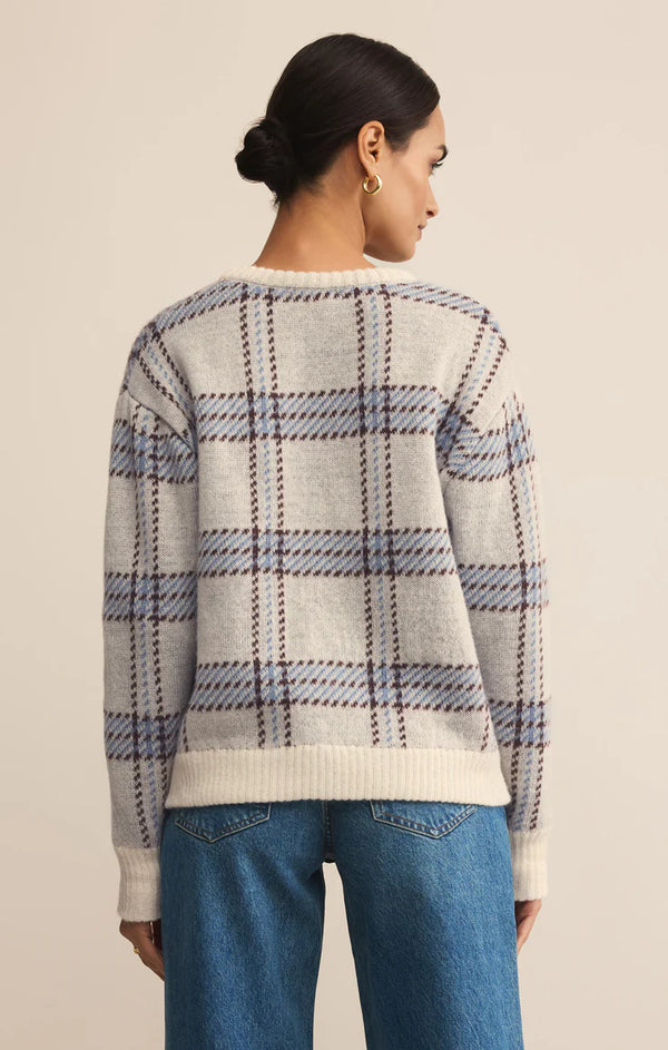 Person wearing a plaid sweater and blue jeans on a beige background