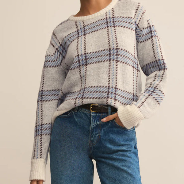 Woman wearing a plaid sweater and blue jeans against a beige background