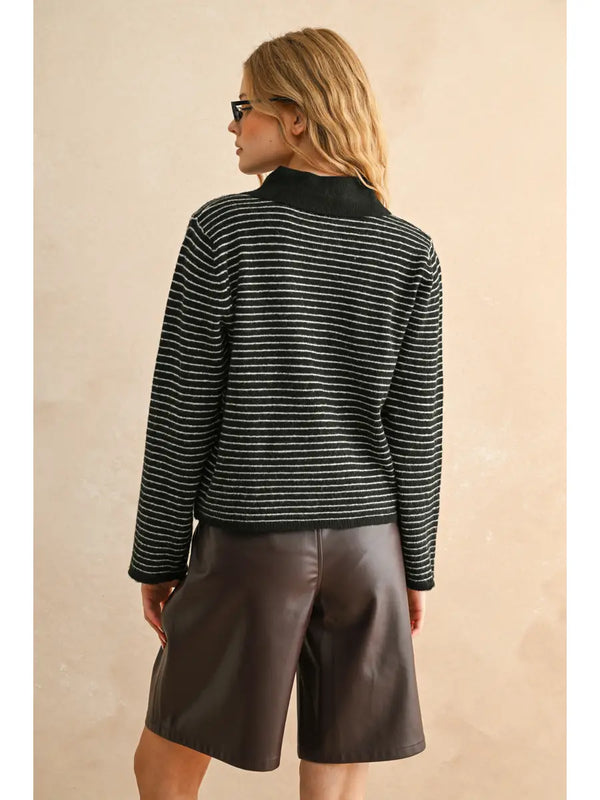 Person wearing a striped sweater and leather shorts against a beige background