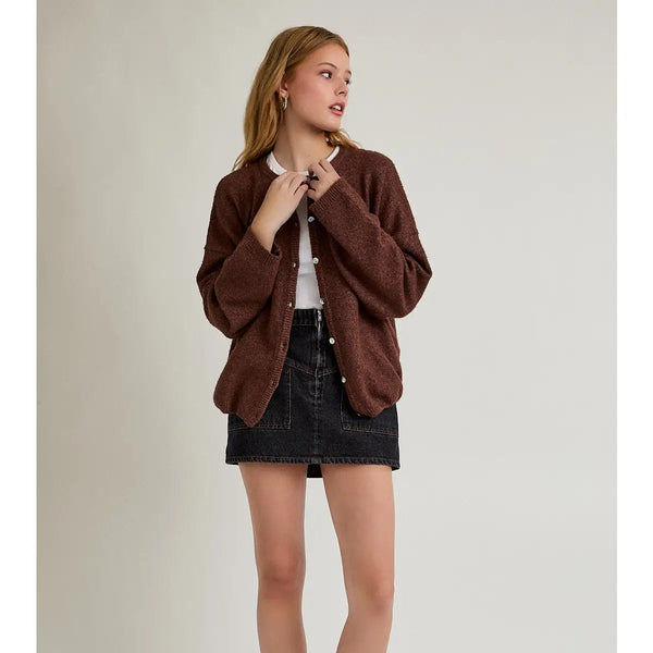 front view of the model wearing a brown cardigan. shows the button down closure. also shows the black denim skirt she is wearing on a beige background.